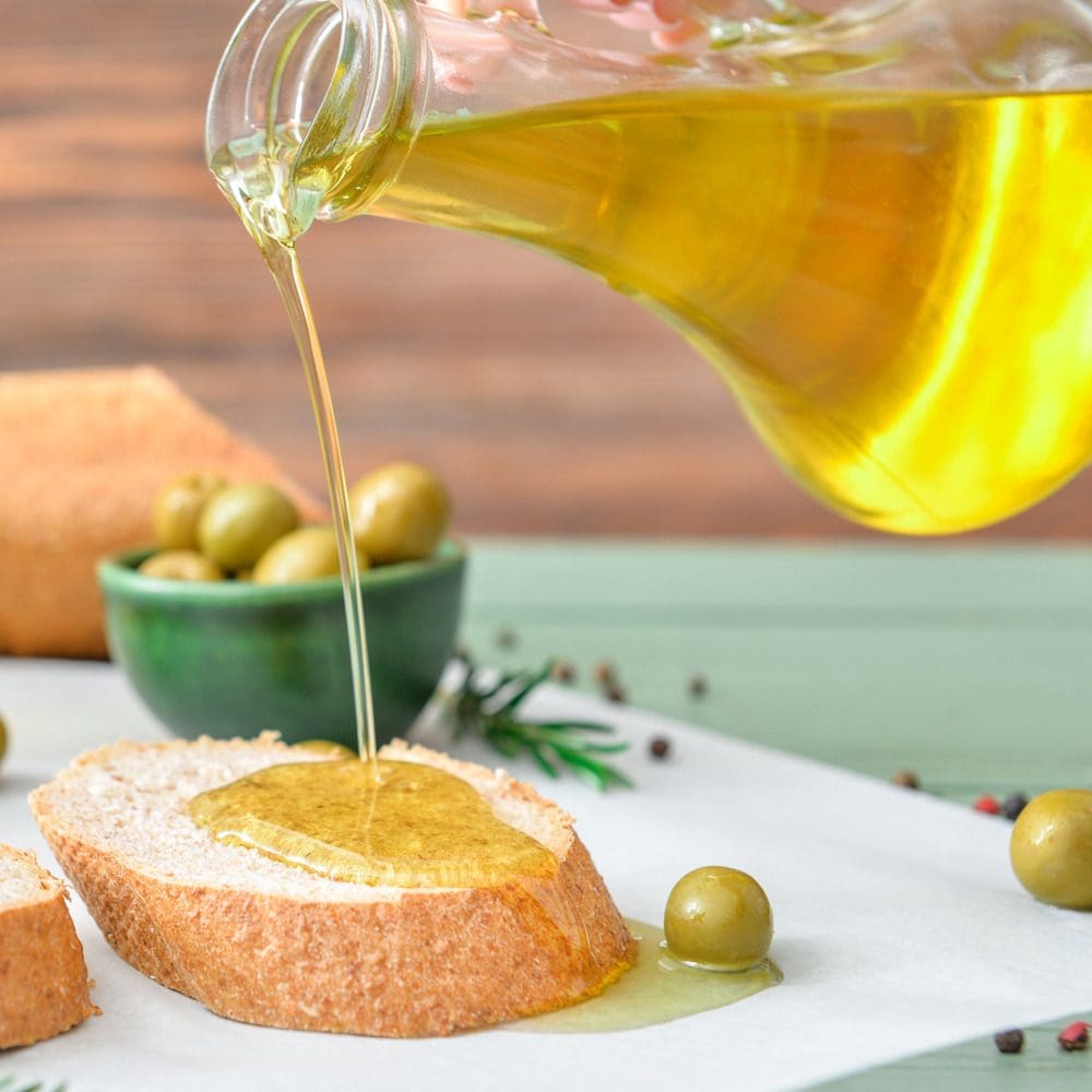 Pouring of tasty olive oil from bottle on fresh bread